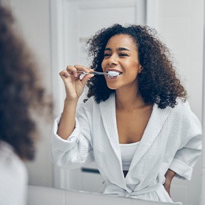 A young woman brushing her teeth in front of a bathroom mirror